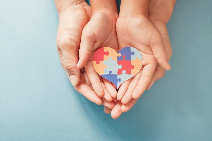 adult and child hands holding autism puzzle heart