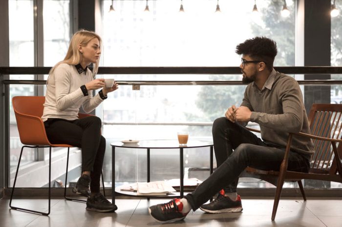 two people sitting at a table in a cafe talking to each other