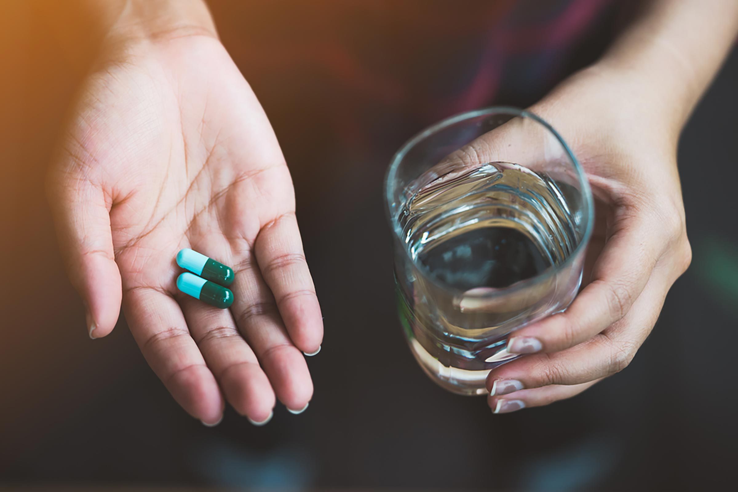 hand holding magnesium capsules and glass of water