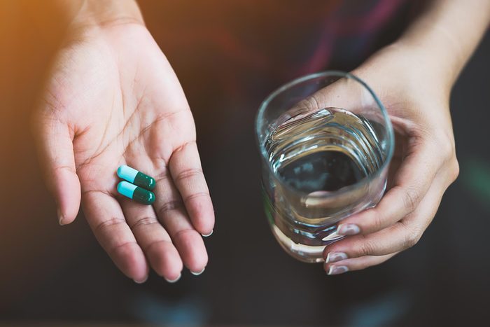hand holding magnesium capsules and glass of water
