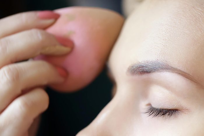A woman applying foundation to her forehead with a pink beauty blender.