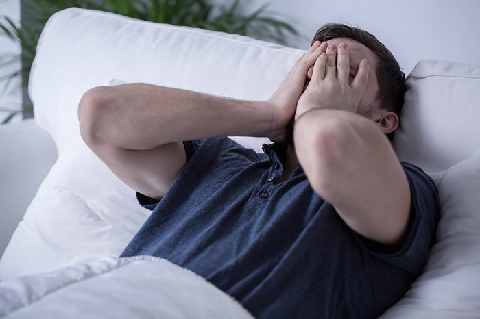 man in bed with hands over face