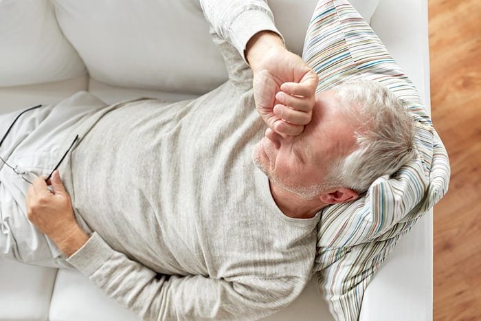 older man on couch sleeping with hand to head