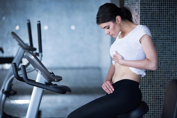 woman looking at her own abs while sitting in gym
