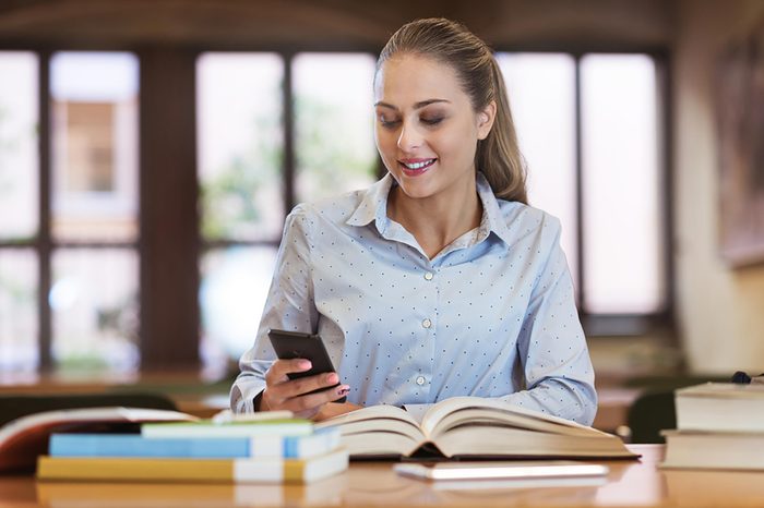 woman looking at phone with books in front of her