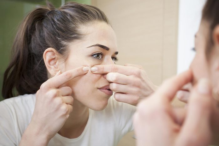 woman popping pimple in mirror