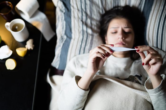 woman sick in bed looking at thermometer