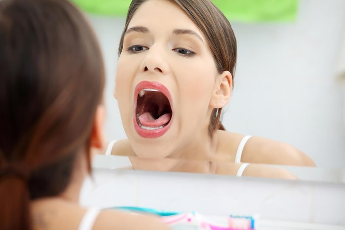 woman looking at open mouth in mirror
