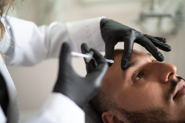 plastic surgeon injecting man's face with filler botox