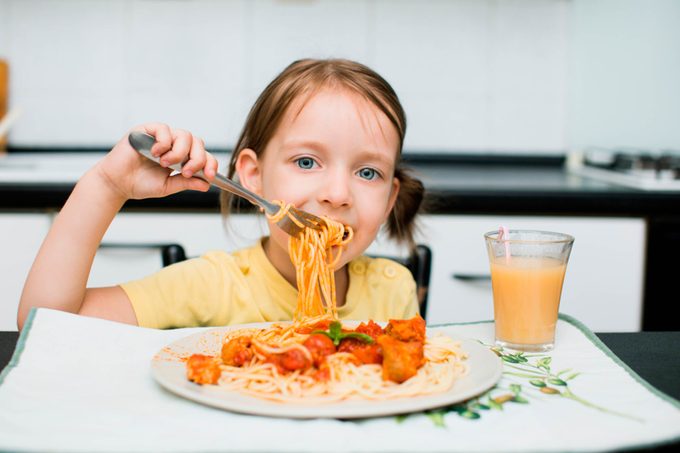 young girl eating spaghetti with meatballs and orange juice