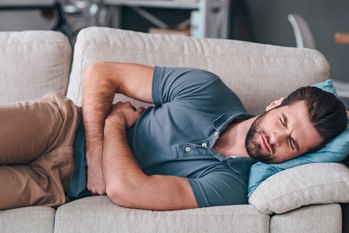man clutching stomach lying on couch