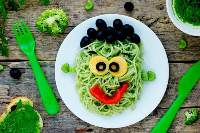 green pasta with a smiley face (yolk eyes, red pepper mouth, and olive hair)