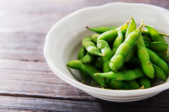 edamame pods in a white bowl on wood surface