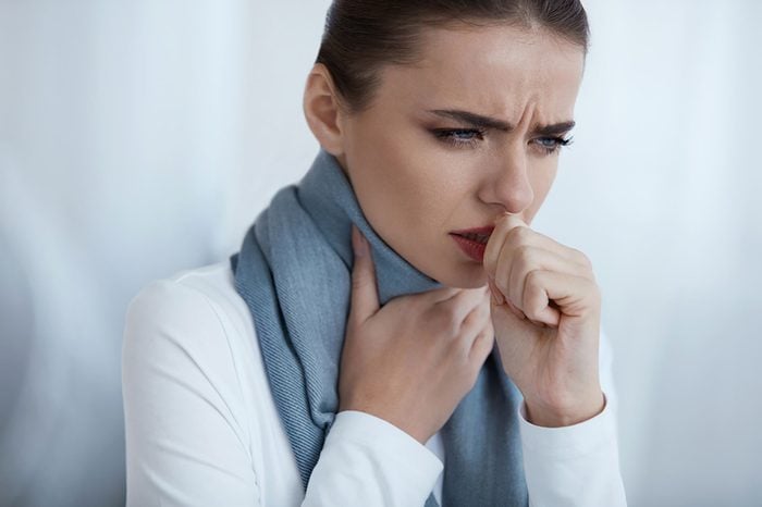 woman with one hand on her throat, and coughing into the other