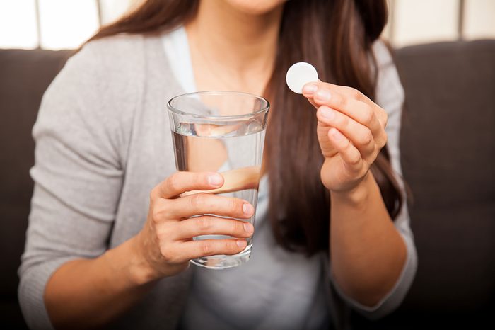 woman holding a glass of water and an antacid wafer