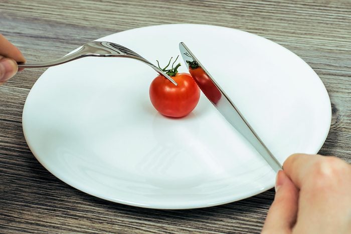 person using a knife and fork to eat a cherry tomato on a white plate