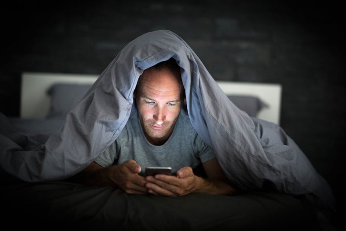 man under bed covers looking at phone