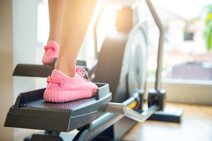 Woman in pink sneakers using the elliptical.