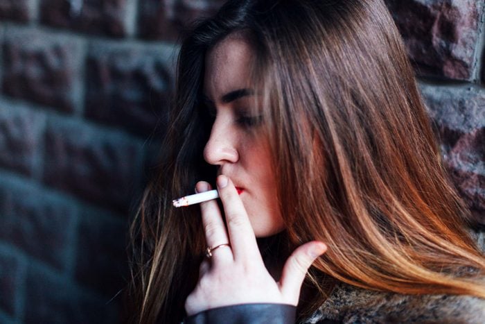 close up of woman smoking while standing against a brick wall, moody lighting