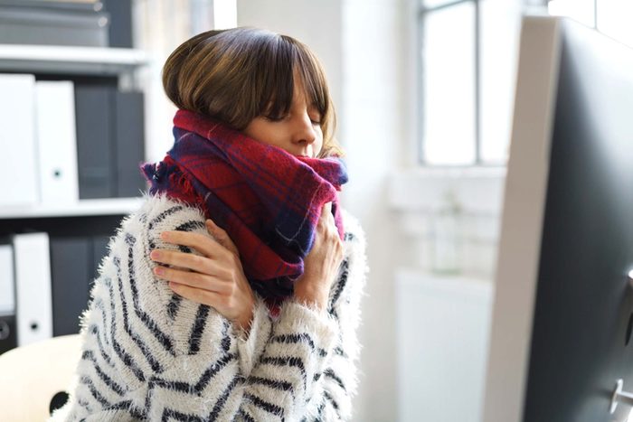 woman indoors wrapped in a scarf, chilled