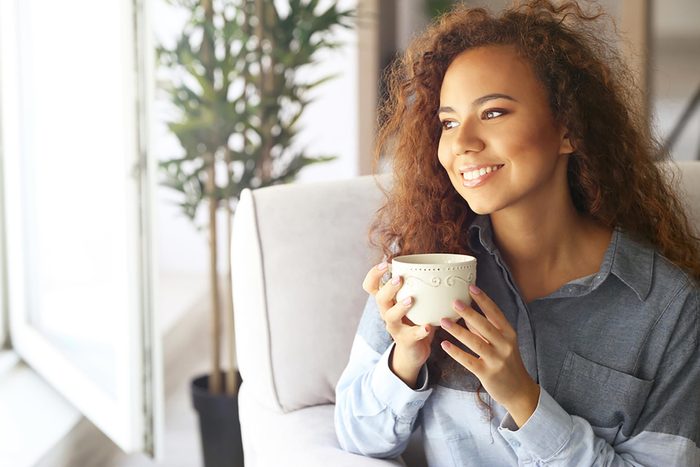 woman staring out a window and smiling with a coffee
