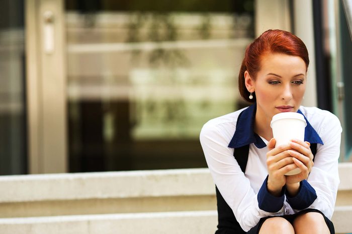 woman seated outdoors holding a coffee cup with a stressed expression on her face
