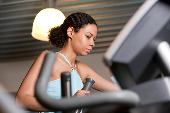 Woman in a blue tank top working out on an elliptical.