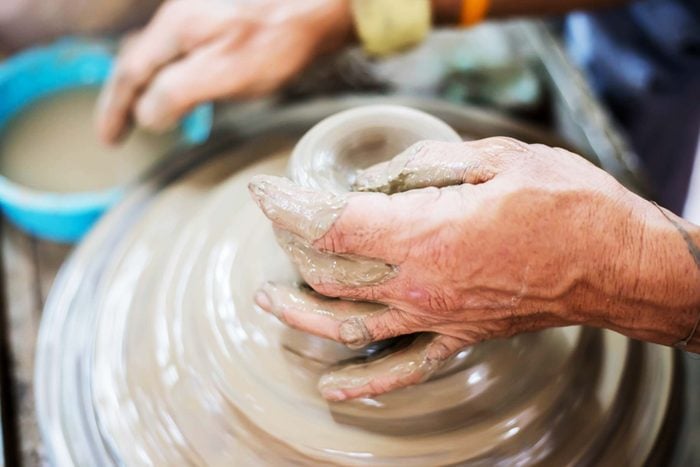 mature hands crafting a ceramic vessel on a pottery wheel