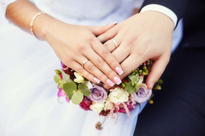hands of a bride and groom with wedding rings on on top of the wedding bouquet