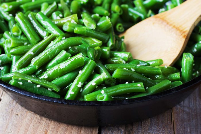 bowl of green beans and wooden serving spoon on wooden surface