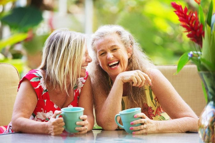 two mature woman laughing and holding coffee mugs
