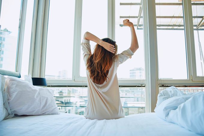 woman waking up and stretching on the side of her bed