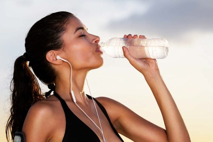woman with earbuds in workout gear, drinking from a bottle of water