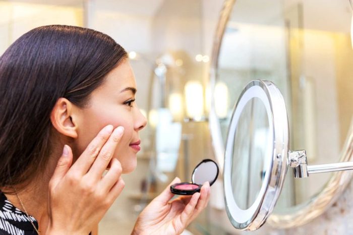 Asian woman applying makeup in a mirror