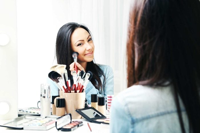 Woman applying makeup to her face in front of a mirror.