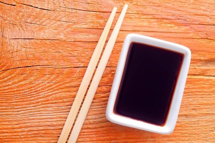 soy sauce in a white dish next to chopsticks on a wood table 