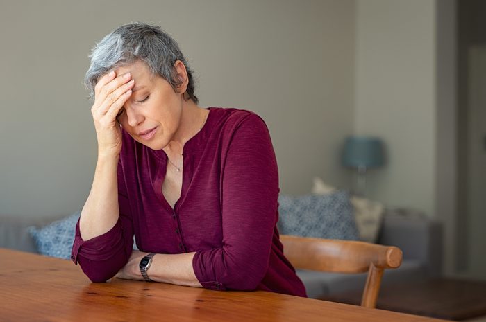 senior woman sitting at table with headache