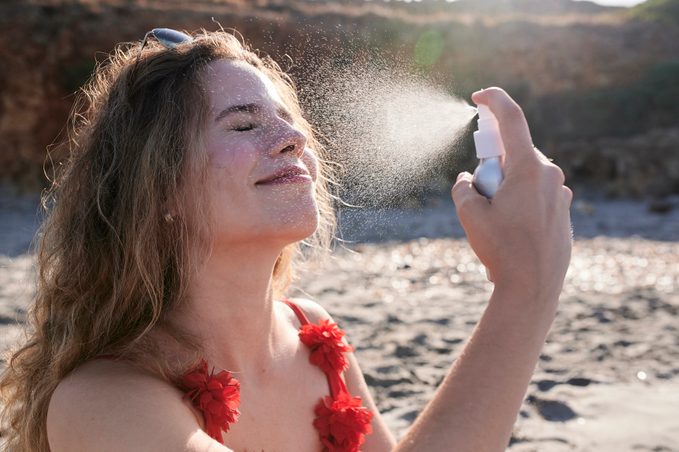 woman spraying sunscreen on face at the beach