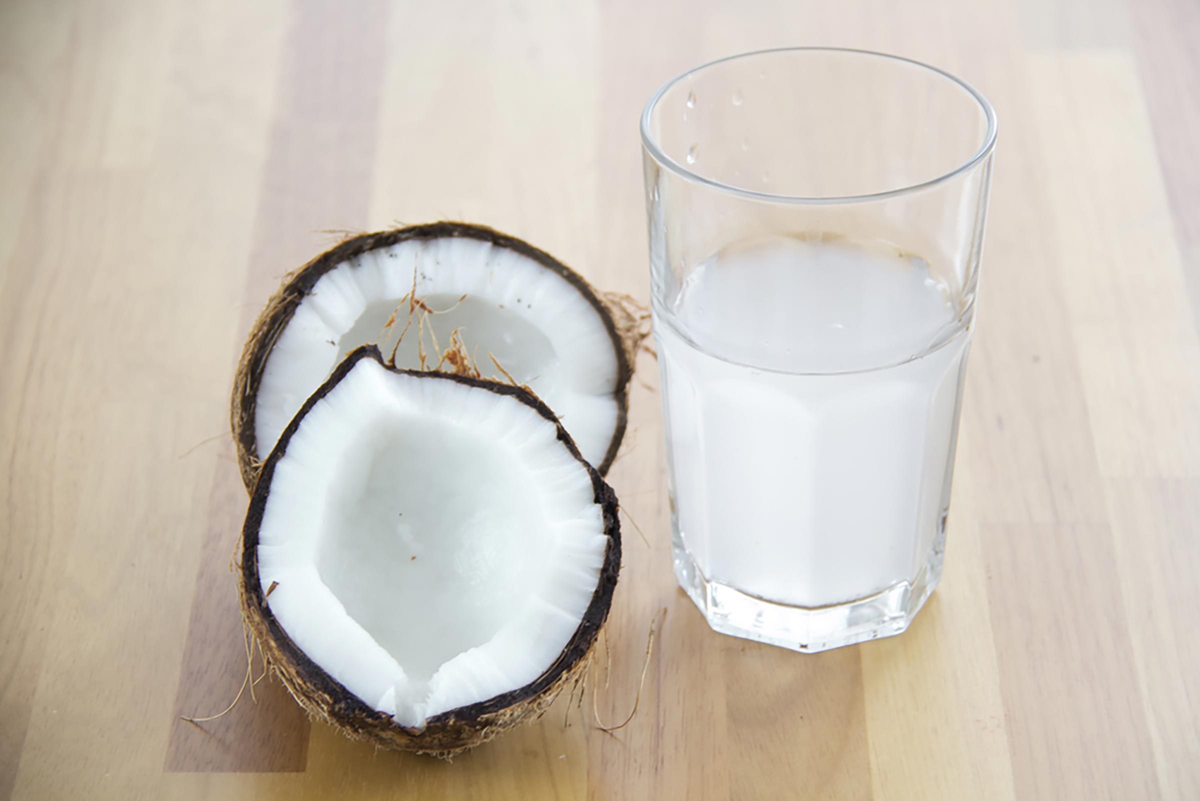 Glass of coconut water next to two halves of a coconut