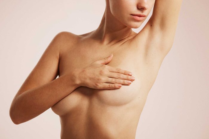 woman's naked torso with arm and hand covering breasts