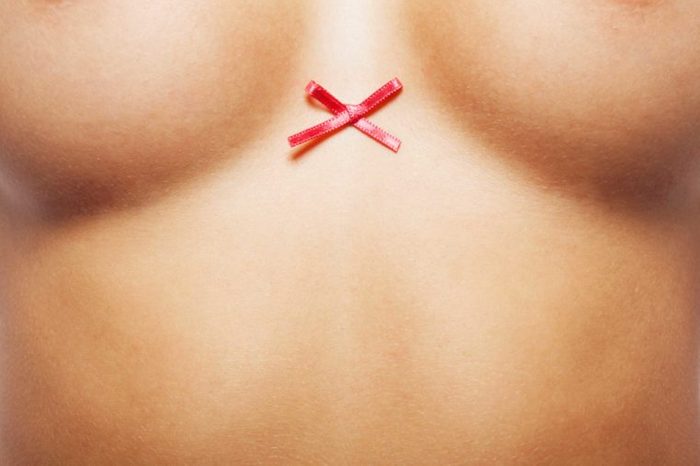 close up of woman's naked torso with cancer ribbon between breasts