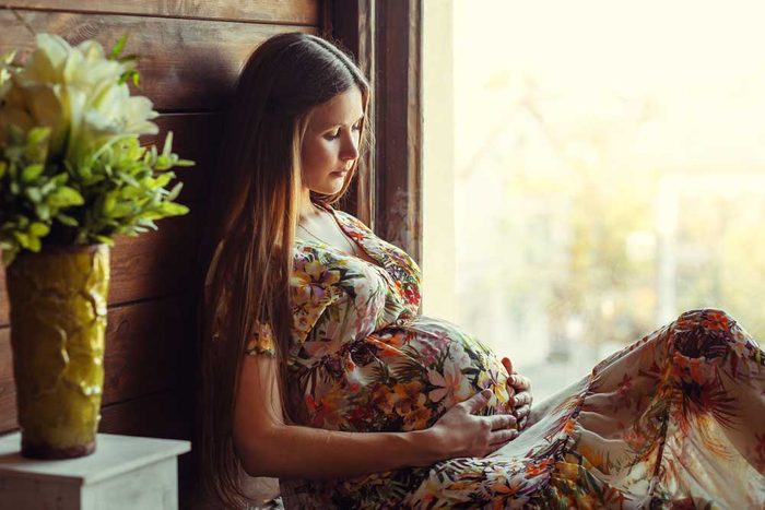 pregnant woman in a flowery dress reclining in a window seat