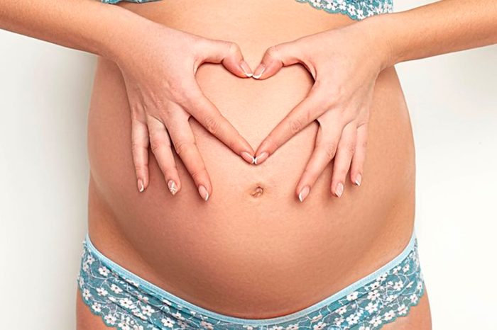pregnant woman's bare belly; she's making a heart out of her fingers over her belly