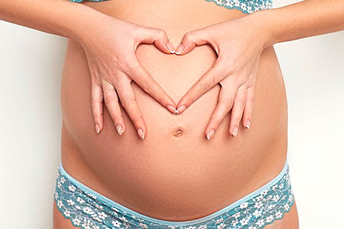 pancia nuda di una donna incinta; sta facendo un cuore con le dita sulla pancia
