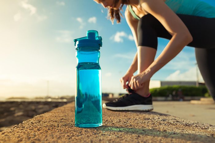 Woman runner tying sneaker next to bottle of water