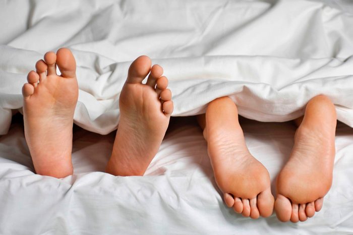 two sets of bare feet in a bed, one pointed up, the others down