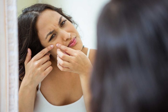 woman looking in mirror and popping a pimple