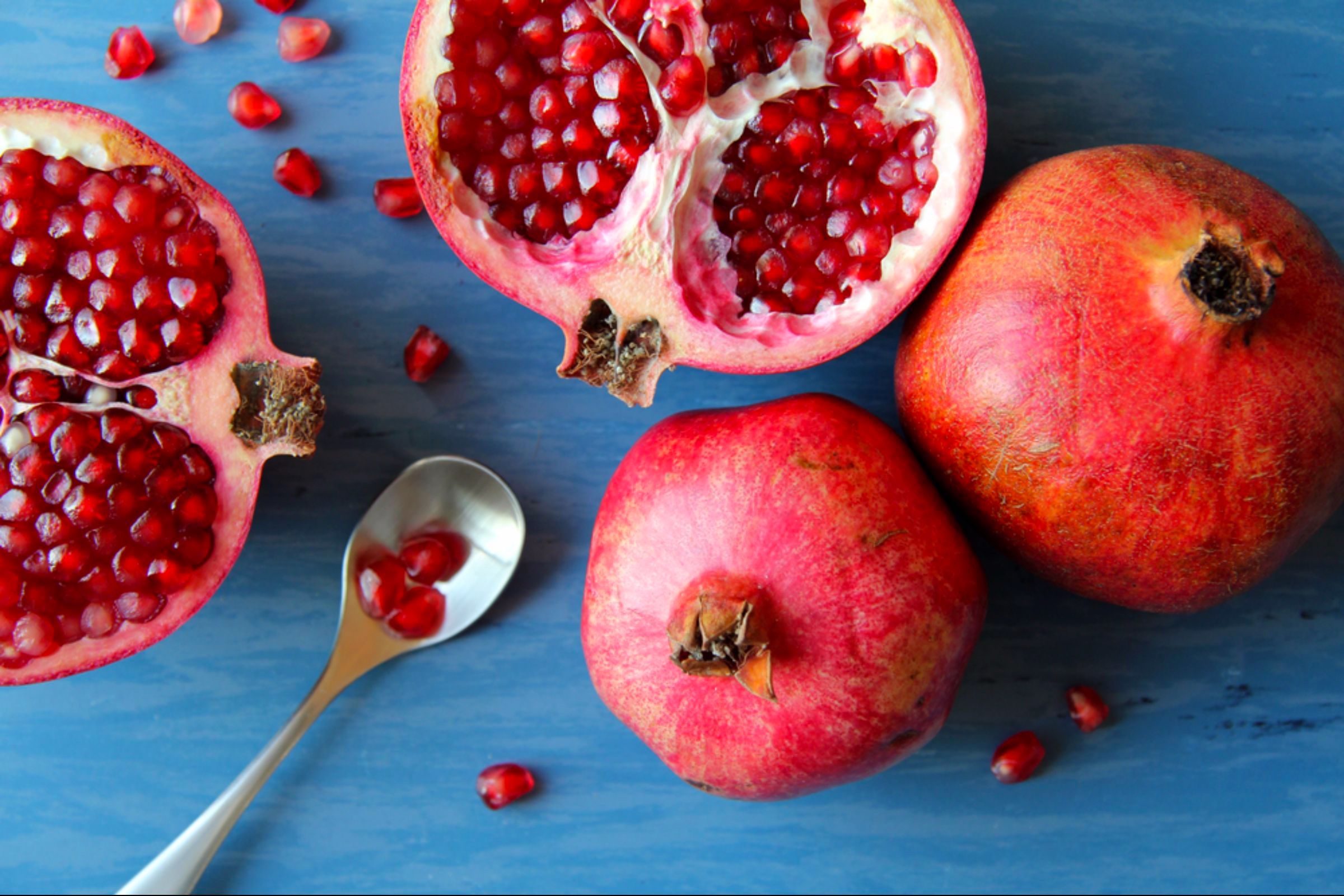 whole and halved pomegranate, spoon full of pomegranate seeds