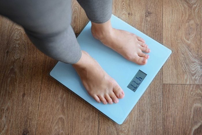 Woman in yoga pants weighing herself on a blue scale.