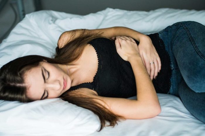 Woman lying in bed holding her arms across her body to ease the cramps.